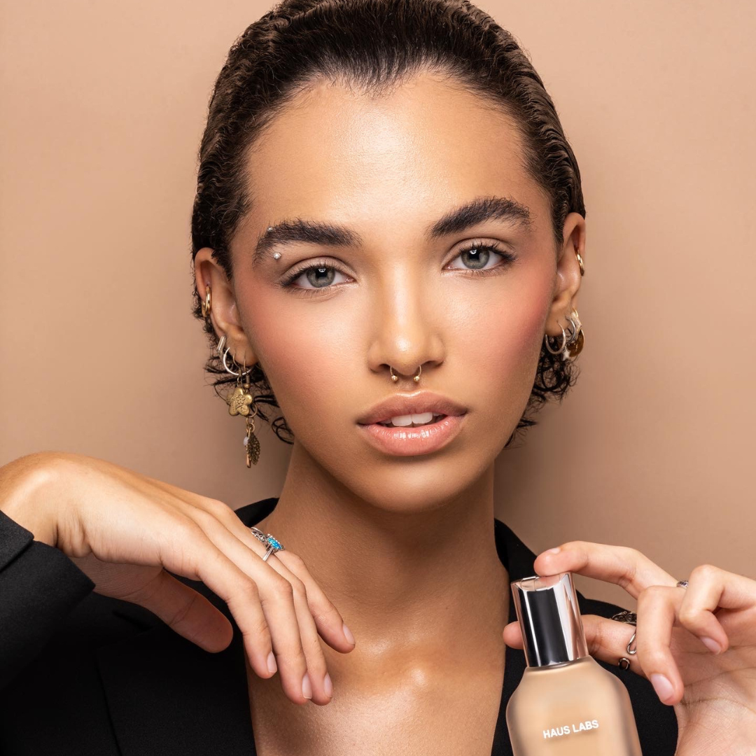 Model with makeup and piercings holding Haus Labs foundation bottle