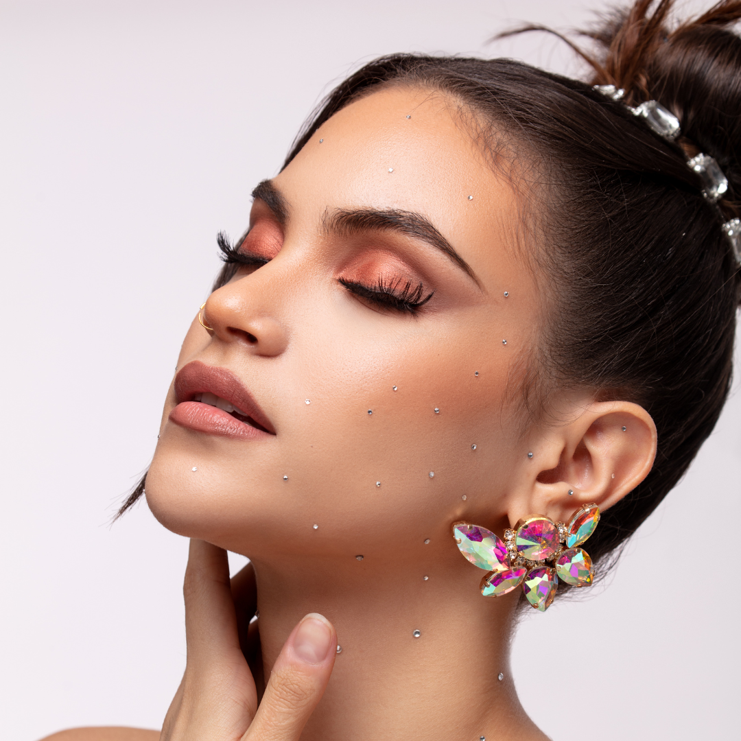 Woman with sparkling makeup, butterfly earrings, and closed eyes