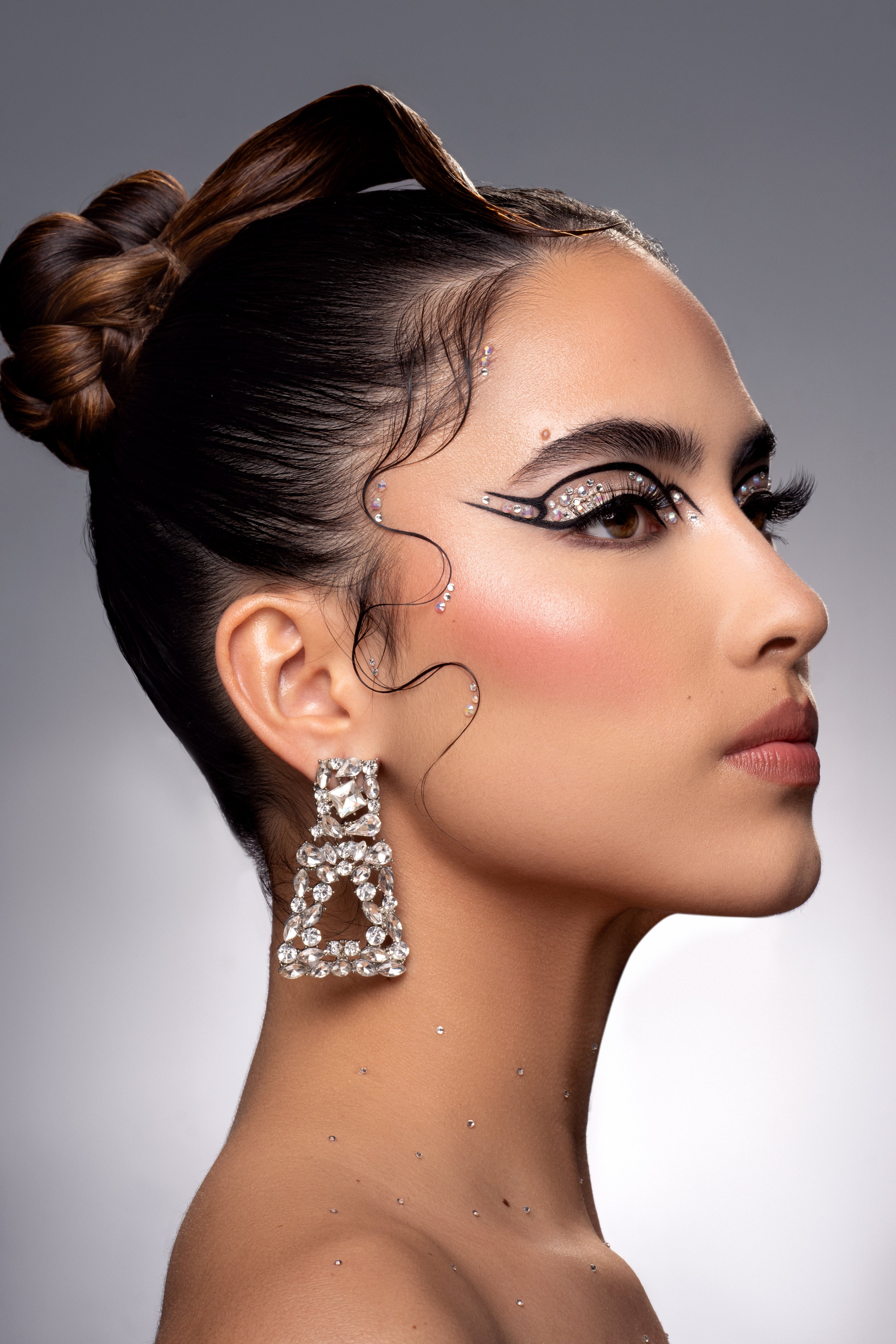 Side profile of woman with elaborate crystal makeup and large diamond earrings